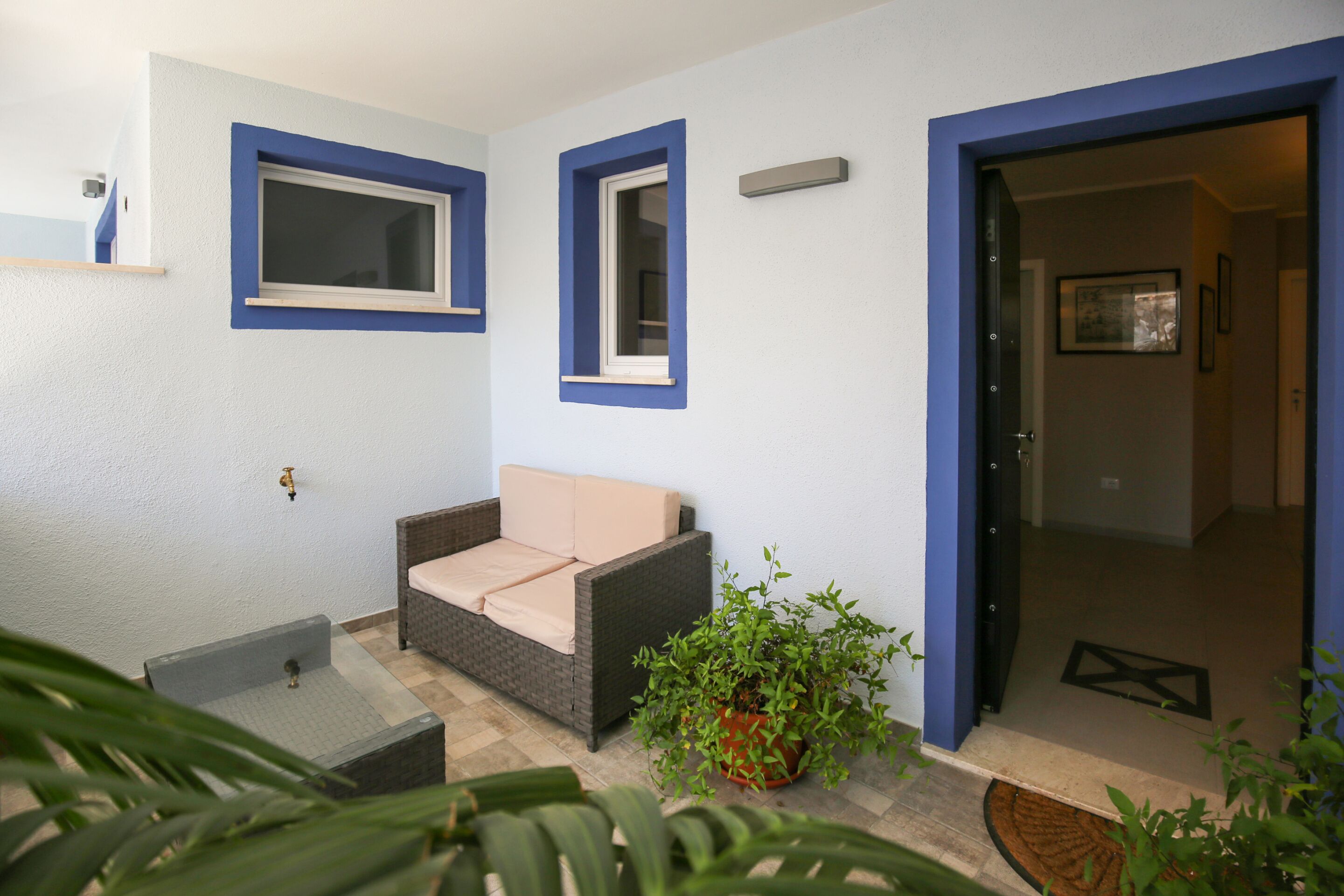 A room with a sofa, a small table, a potted plant, and a door leading to another room.