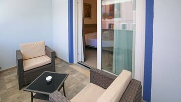 A balcony with wicker furniture, a small table, and a sliding glass door leading to a bedroom.