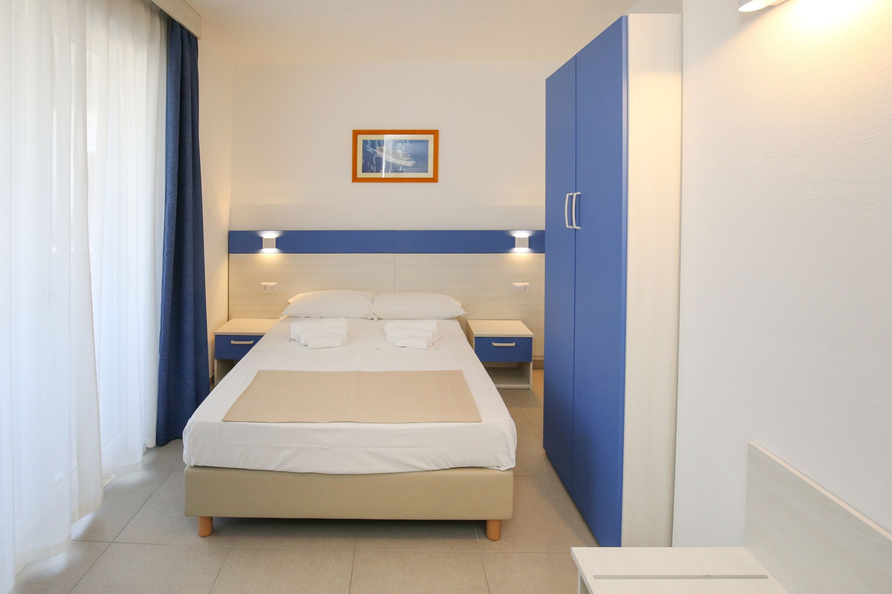 Habitación de hotel con cama, mesitas de noche, armario y un cuadro en la pared.