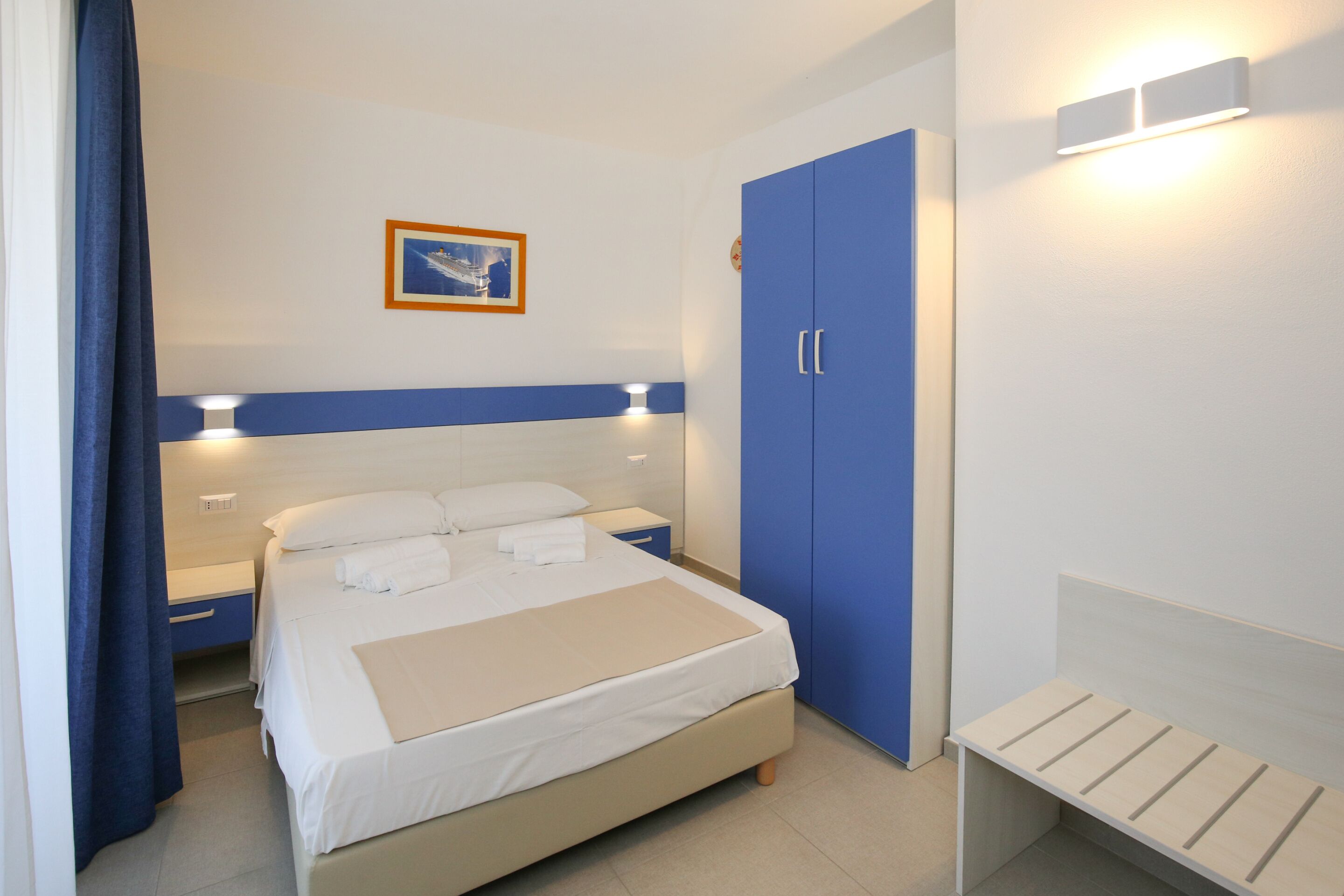 Une chambre bien rangée, avec un lit, des tables de chevet, une armoire et un banc.