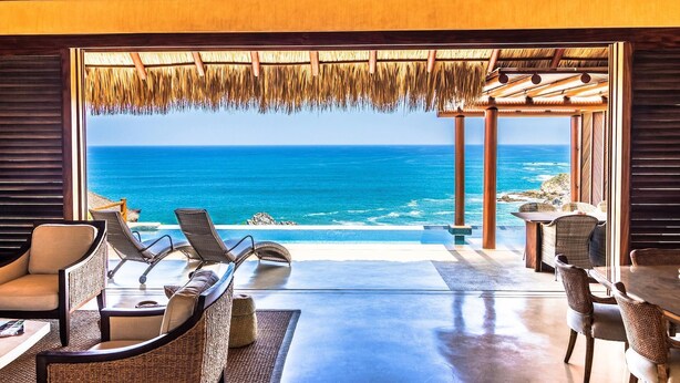 A room with a view of the ocean, furnished with wicker chairs and a table, and a thatched roof. - Villa Maroma (Santa María Huatulco)