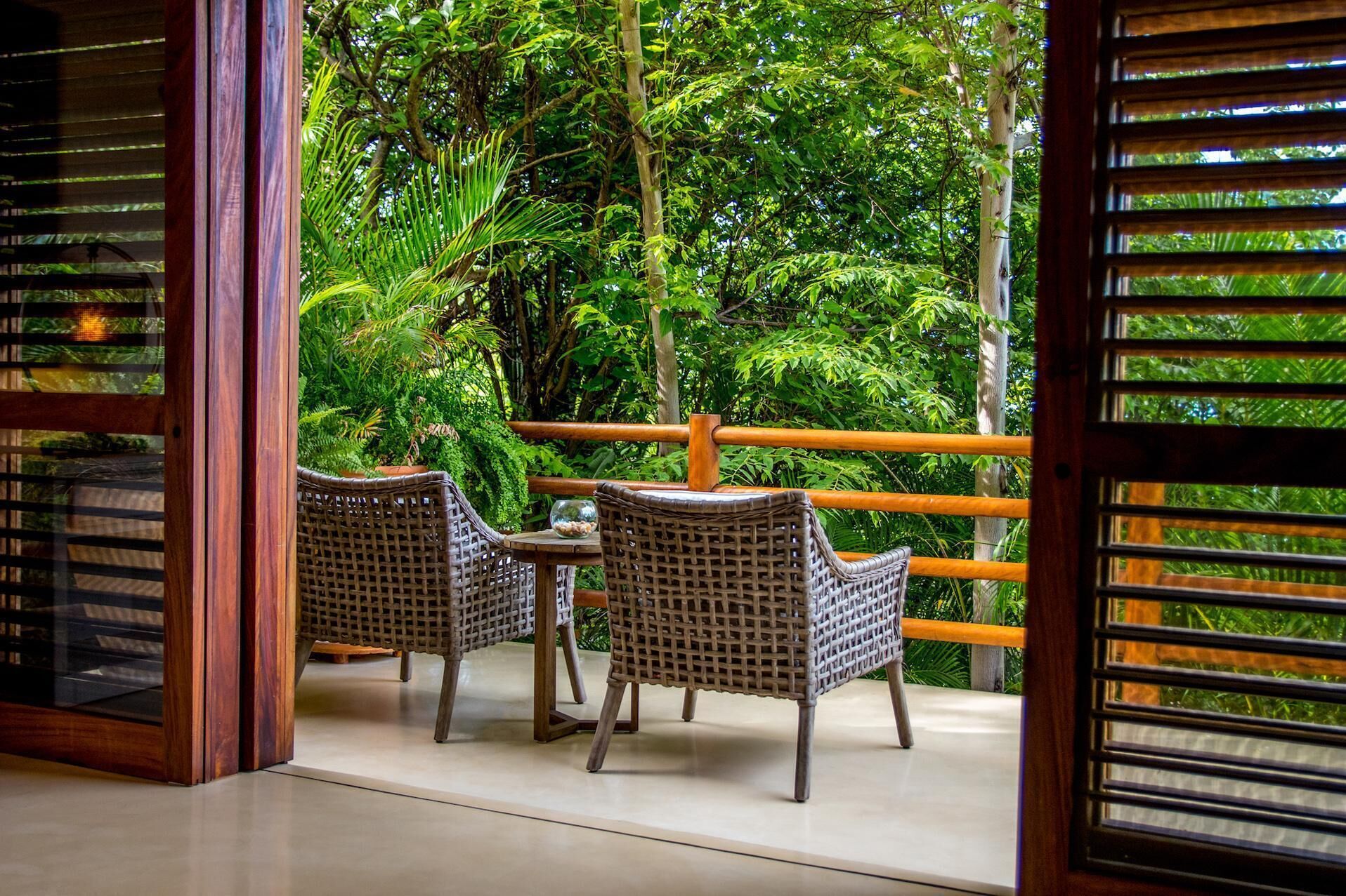Un balcon agrémenté de fauteuils en osier et d’une petite table, donnant sur un jardin luxuriant.