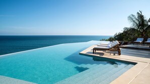 A infinity pool with clear blue water, lounge chairs, and a view of the ocean. - Villa Maroma (Santa María Huatulco)