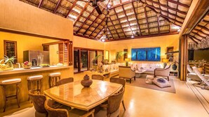 A spacious living area with a high ceiling, a dining area with a glass table, and a bar area with stools. - Villa Maroma (Santa María Huatulco)