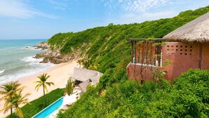 Een strandhuis met een zwembad, overkappingen met rieten daken en weelderige begroeiing.