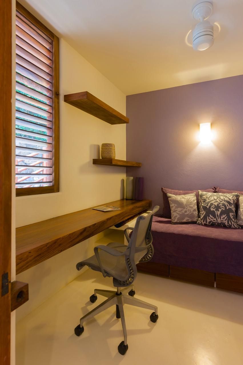 Une pièce comprenant un bureau, une chaise, des étagères, un canapé et une fenêtre avec des stores.