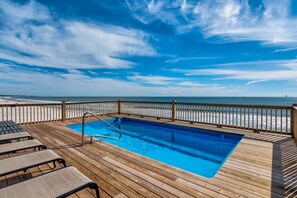 Eine Holzterrasse mit Swimmingpool, Blick auf den Strand und Liegestühlen.