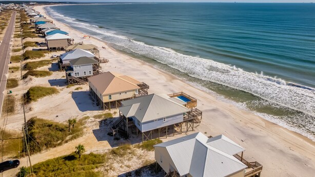 A beachfront property with multiple houses, some with elevated decks, and a beach in the background. - Encantado | Cancellation 9/26 week. Pool! (Dauphin Island)