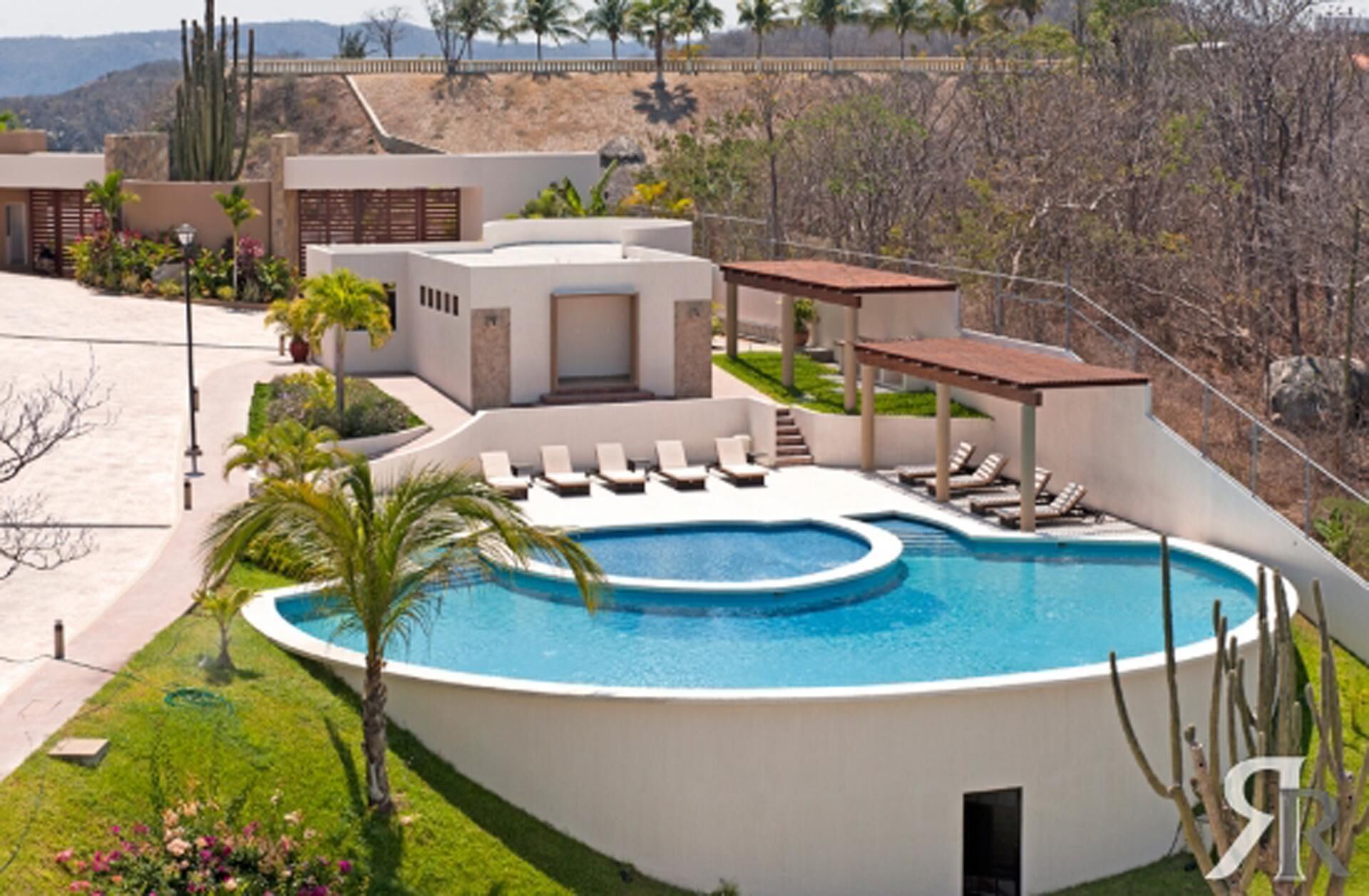 A modern pool area with a curved design, surrounded by lounge chairs and a small garden.