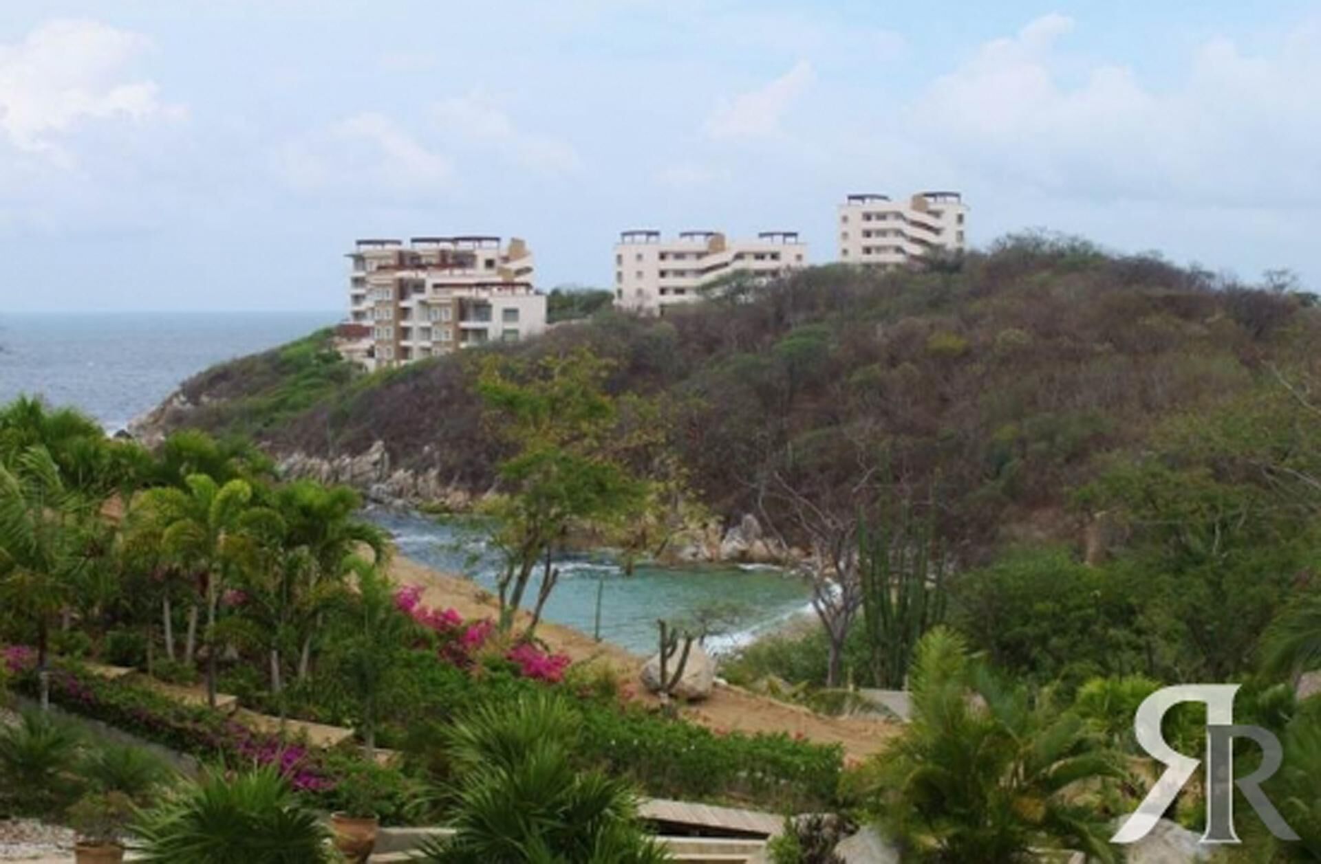 A coastal view with buildings on a hillside, a beach, and lush greenery.