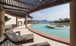 A pool area with a curved design, lounge chairs, and a view of the sea.