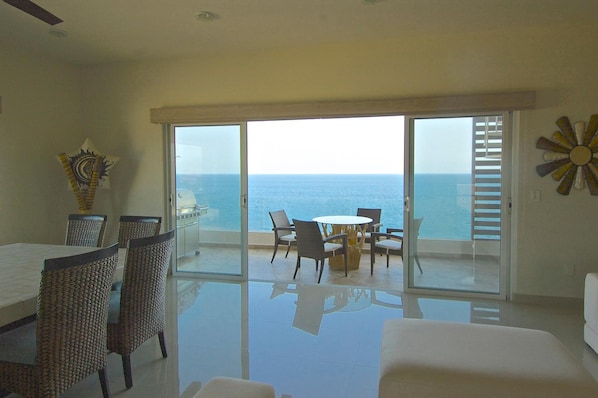 A balcony with a view of the ocean, a dining area with wicker furniture, and a ceiling fan.