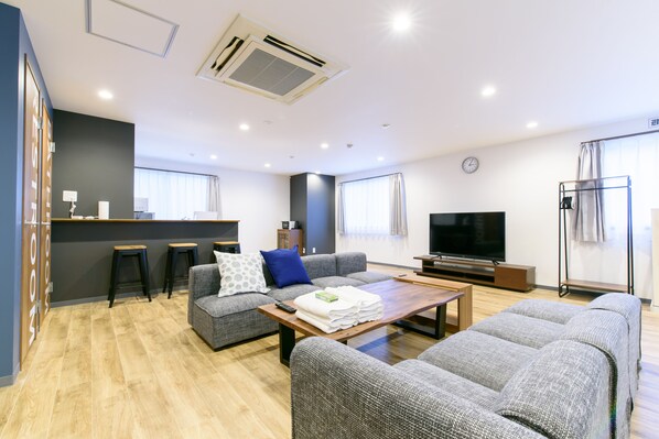 Una sala de estar moderna con un sofá, sillas, una mesa de centro, un televisor y una zona de cocina con taburetes.