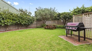 A backyard with a barbecue grill, picnic table, and a wooden fence. - Scenic Beach Apartment (Apollo Bay)