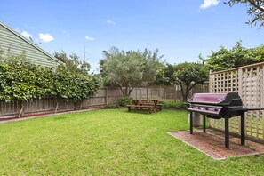 Ein Garten mit Grill, Picknicktisch und Holzzaun.