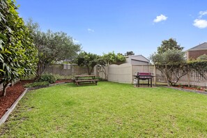 A backyard with a wooden bench, a barbecue grill, and a shed. - Scenic Beach Apartment (Apollo Bay)