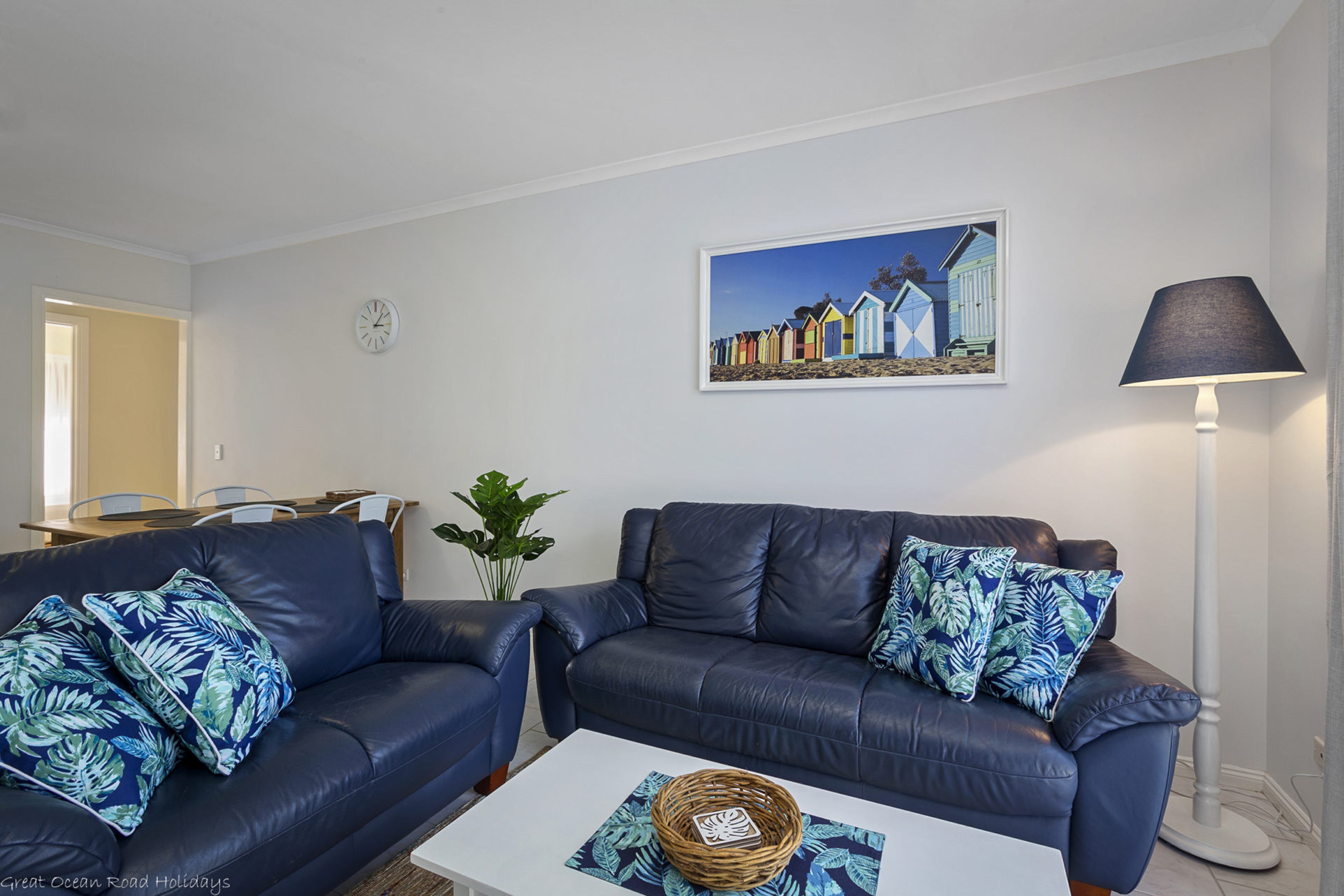 A living room with two dark sofas, a coffee table, a lamp, a painting, and a plant.