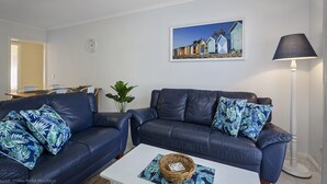 A living room with two dark sofas, a coffee table, a lamp, a painting, and a plant. - Scenic Beach Apartment (Apollo Bay)