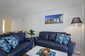 Ein Wohnzimmer mit zwei dunklen Sofas, einem Couchtisch, einer Lampe, einem Gemälde und einer Pflanze.