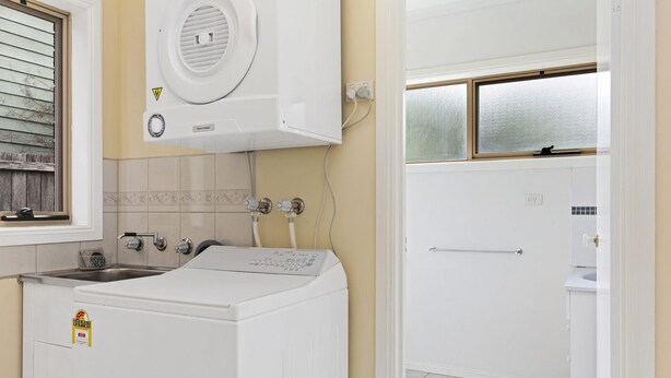 A laundry room with a front-loading washer and dryer, a sink, and a window with frosted glass. - Scenic Beach Apartment (Apollo Bay)