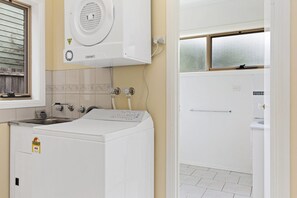 A laundry room with a front-loading washer and dryer, a sink, and a window with frosted glass.
