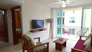 A living room with a TV, wooden furniture, a balcony with chairs, and a ceiling fan. - Terrazas C7 (Santa María Huatulco)