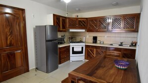 A kitchen with wooden cabinets, a refrigerator, stove, and a dining table with chairs. - Terrazas C7 (Santa María Huatulco)