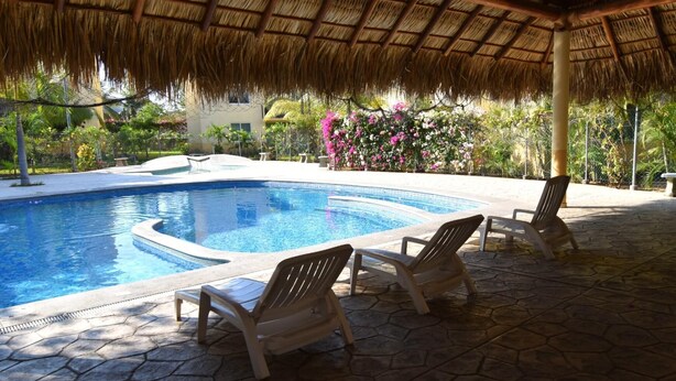 A swimming pool with a thatched roof overhead, surrounded by stone tiles and equipped with lounge chairs. - Terrazas C7 (Santa María Huatulco)