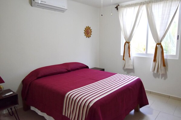 A bedroom with a bed, a nightstand, a wall-mounted air conditioner, and a window with curtains. - Terrazas C7 (Santa María Huatulco)