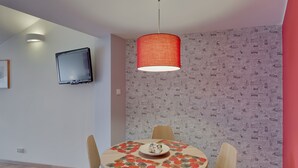 En matplats med ett runt bord, stolar, en röd hänglampa, en väggmonterad TV och en tapet med mönster.