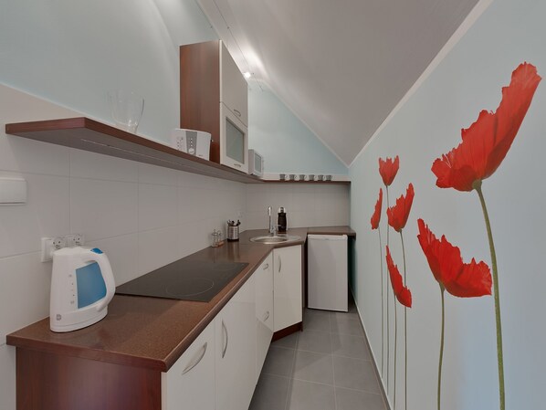 Una cocina moderna con armarios blancos, encimera de madera, microondas integrado y un refrigerador pequeño.