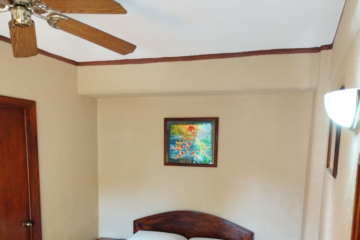 A bedroom with a bed, nightstand, ceiling fan, and a framed picture on the wall.