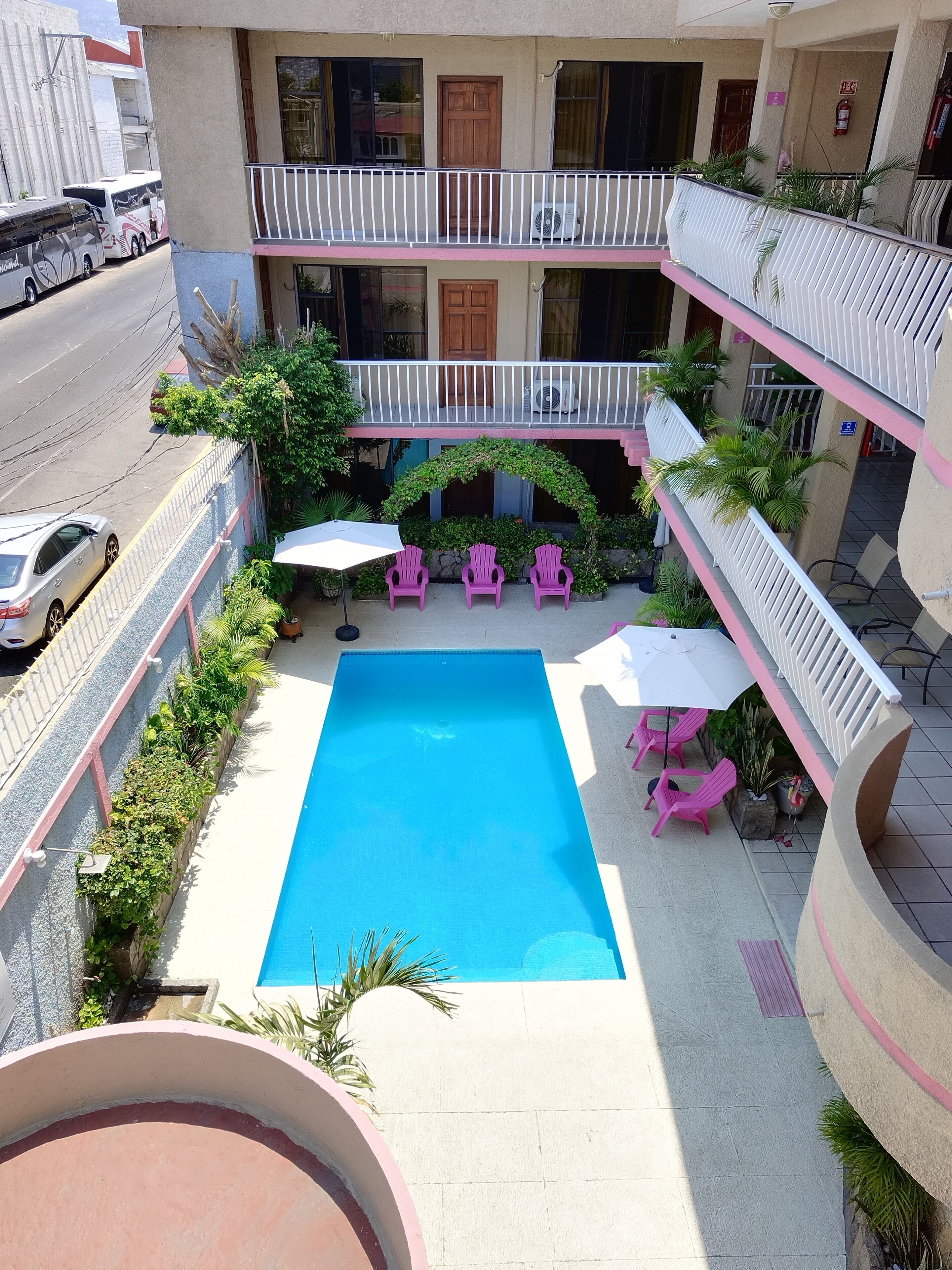 A hotel with a central pool, outdoor seating, and a multi-level balcony.