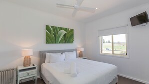 Ein Schlafzimmer mit Bett, Deckenventilator, Fenster mit Aussicht und einem Bild an der Wand.