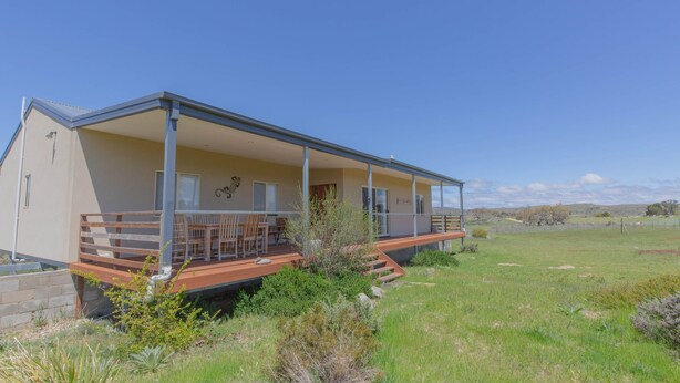Ein modernes Einfamilienhaus mit überdachter Veranda, einer kleinen Terrasse und einem Rasen.