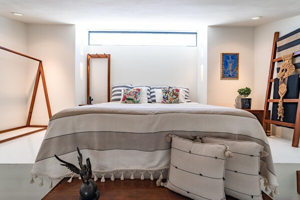 A modern bedroom with a large bed, striped bedding, and a small plant on the nightstand.