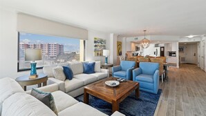 Ein modernes Wohnzimmer mit einer Couch, Sesseln und einem Couchtisch. Im Hintergrund ist eine Küche zu sehen.
