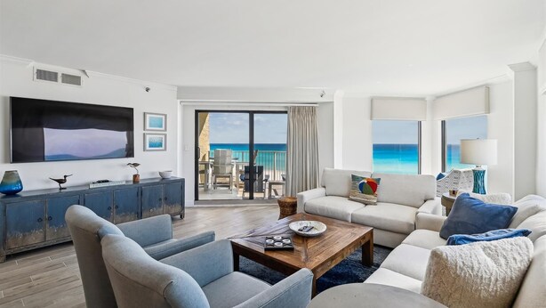 Ein modernes Wohnzimmer mit großem Fernseher, bequemen Sitzmöglichkeiten und Meerblick.