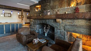 A stone fireplace with a mantel displaying various items and a seating area with two armchairs and a small table. - Piscine + Casiers à Ski | 50m des Remontées ! (Saint-Lary-Soulan)