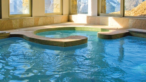 A pool with a stone border and a view of mountains through large windows. - Piscine + Casiers à Ski | 50m des Remontées ! (Saint-Lary-Soulan)