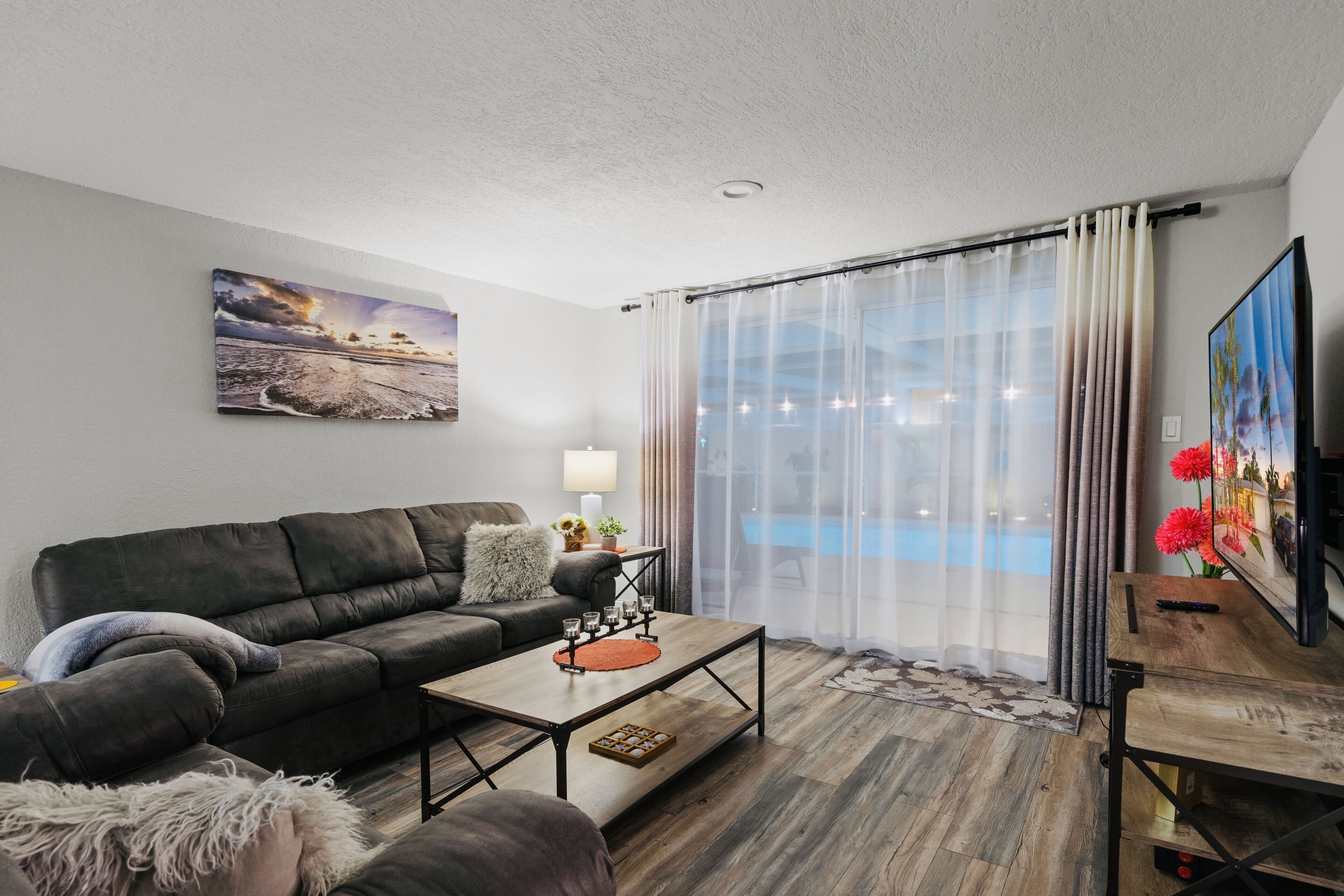 A modern living room with a sofa, coffee table, and a painting of a beach scene.