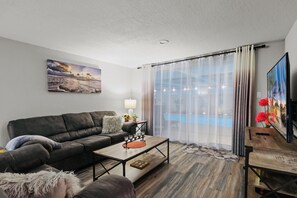 A modern living room with a sofa, coffee table, and a painting of a beach scene. - 🌴 Great escape with private heated pool LOOK INSIDE  (Port Richey)