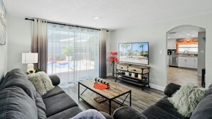 A modern living room with a sofa, coffee table, and TV. There is a kitchen in the background. - 🌴 Great escape with private heated pool LOOK INSIDE  (Port Richey)