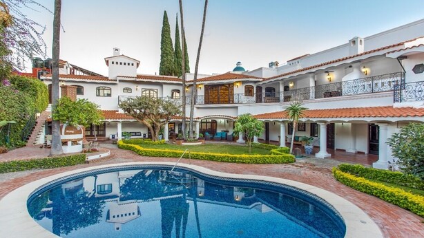 Una gran piscina rodeada por un patio con varios edificios, incluyendo una estructura de dos pisos con balcones y un porche cubierto.