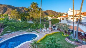 Una piscina rodeada de exuberante vegetación y montañas al fondo.