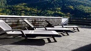 A rooftop terrace with lounge chairs and a view of a forested mountain range. - Apartment 424 with indoor pool (Bad Reichenhall)