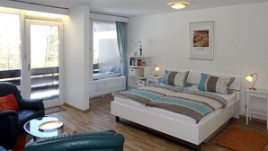 A modern bedroom with a large bed, a seating area with a chair and table, a window with curtains, a radiator, and a small bedside table with a lamp. - Apartment 424 with indoor pool (Bad Reichenhall)
