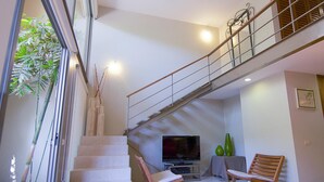 A modern living area with a staircase, a flat-screen TV, two wooden chairs, and a green vase. - Villamar 101 (Santa María Huatulco)