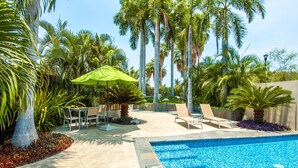 A swimming pool with lounge chairs and a table, surrounded by palm trees and a concrete deck. - Villamar 101 (Santa María Huatulco)