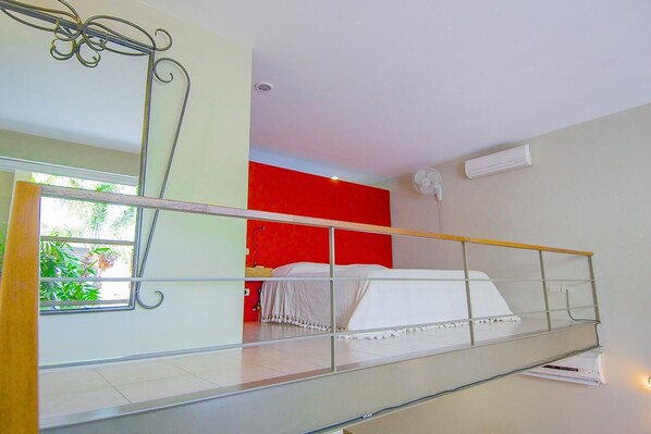 A modern hotel room with a balcony, a red accent wall, and a bed with white bedding.